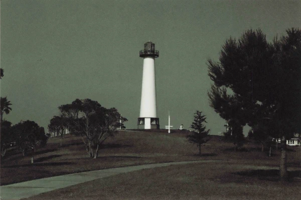 A white lighthouse in a park under a silver sky