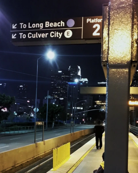 A rail platform at night, signs to Long Beach and Culver City