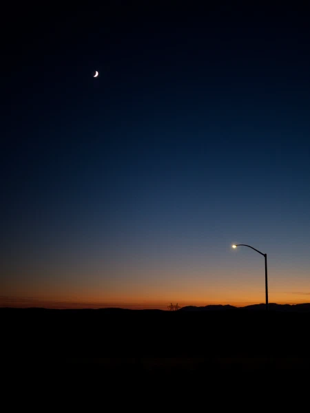 Crescent moon over a twilight gradient with a single streetlamp