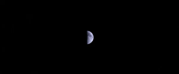 A thin crescent moon alone in a black sky